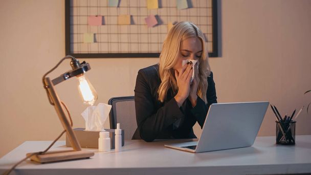 Empresária sofrendo de corrimento nasal perto de pílulas e laptop no escritório  - Foto, Imagem