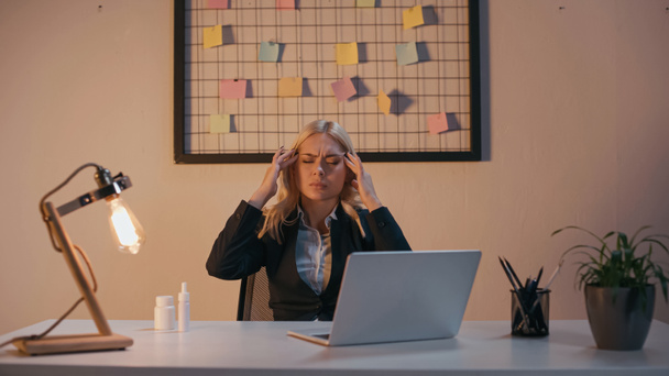 Businesswoman suffering from headache near pills and nasal spray in office in evening  - Fotografie, Obrázek
