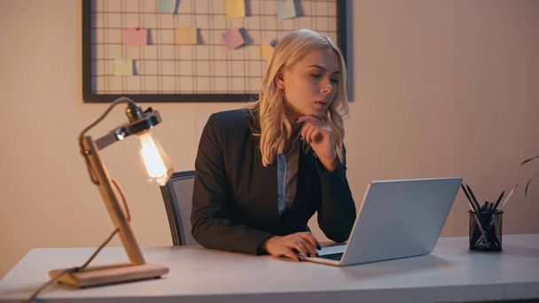 Businesswoman using laptop near lamp on table in office  - Foto, afbeelding