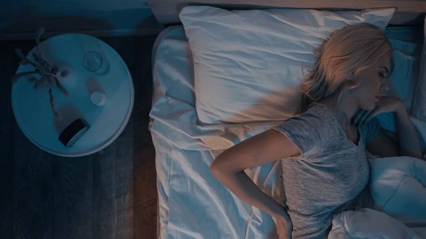 Top kilátás nő alszik az ágyban közelében tabletták az éjjeliszekrényen  - Fotó, kép
