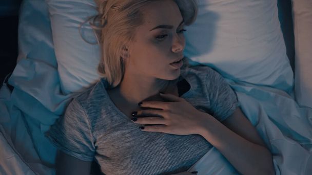 Pohled shora na mladou ženu dotýkající se krku při pocitech bolesti na posteli  - Fotografie, Obrázek