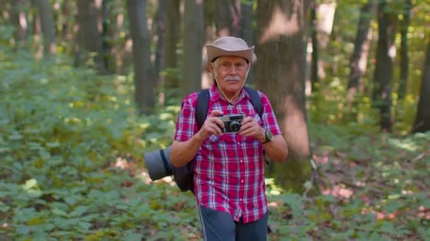 Vanhempi mies isoisä retkellä tutkia villieläinten ottaen kuvia metsässä retro kamera - Materiaali, video