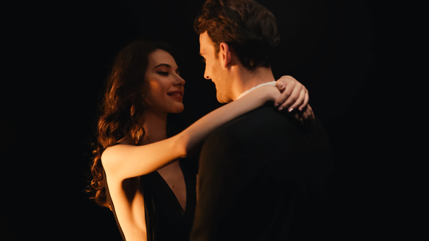Улыбающаяся пара смотрит друг на друга, танцуя медленно, изолированно на черном  - Фото, изображение