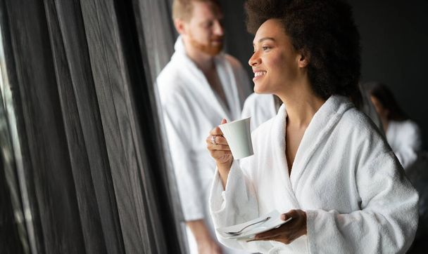 Beautiful woman relaxing at luxury hotel spa wearing bathrobe looking at window and drinking coffee - Foto, afbeelding