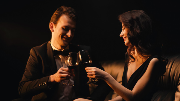 Happy couple clinking glasses of red wine isolated on black - Photo, image