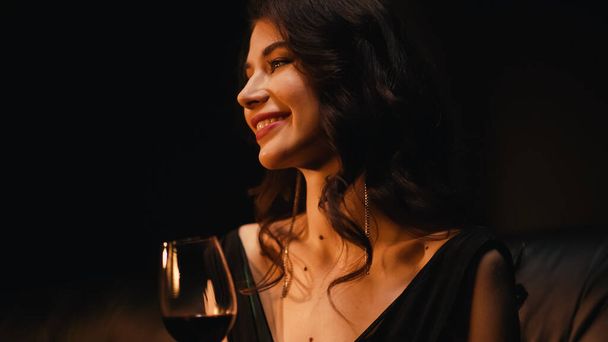 cheerful woman holding glass of wine isolated on black - Foto, Imagen