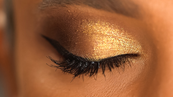 bijgesneden beeld van Afrikaanse Amerikaanse vrouw met gesloten oog en sprankelende gouden oogschaduw - Foto, afbeelding