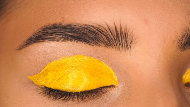 partial view of woman with closed eye and yellow creamy eye shadow  - Foto, immagini