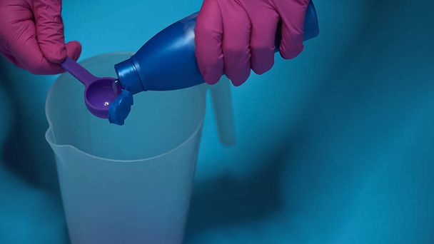 обрезанный вид человека, наливающего жидкость в измерительную ложку на синий - Фото, изображение