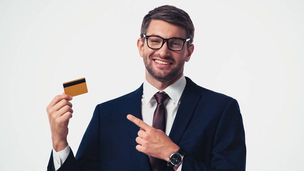 Cheerful businessman in eyeglasses pointing at credit card isolated on white - Fotoğraf, Görsel