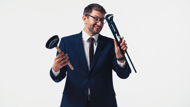 Hombre de negocios sonriente mirando la llave de la tubería y sosteniendo el émbolo aislado en blanco - Foto, imagen