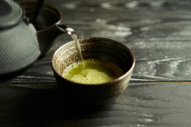 Japoński organiczny matcha zielona herbata w filiżance na czarnym tle drewna. Zdrowy produkt z natury typowej dla orientalnej tradycji. Japońska ceremonia. - Zdjęcie, obraz