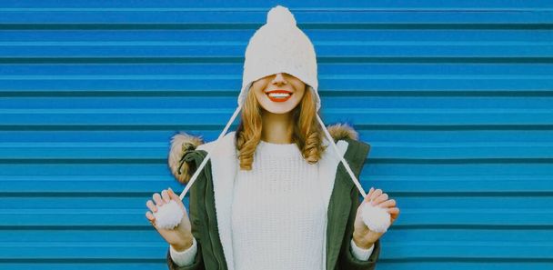 Winter portrait of happy smiling young woman wearing a knitted white hat having fun on blue background - Photo, image
