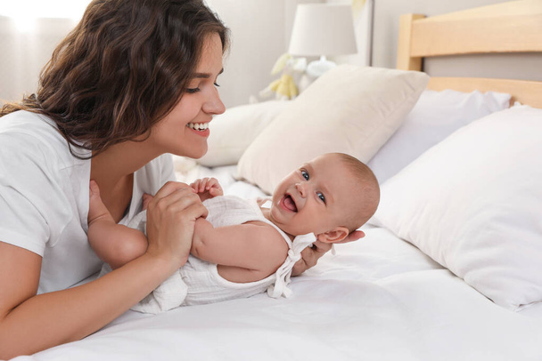 Happy young mother with her cute baby on bed at home - Foto, Imagen