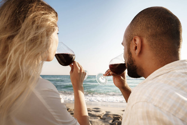 Portrait of a young couple sitting on the beach and drinking wine - Φωτογραφία, εικόνα