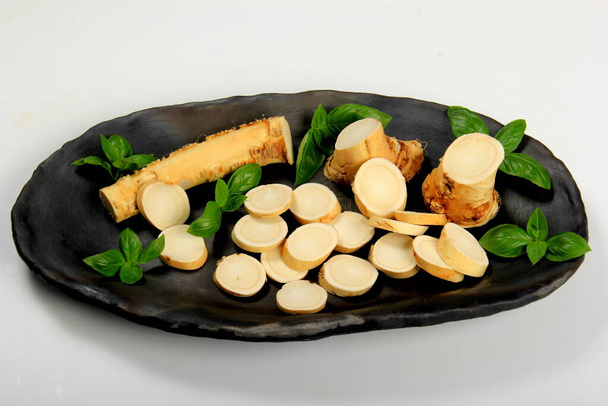 Cut Horseradish roots or taproot on an black clay plate. White background. Fresh horseradish.  - Photo, Image