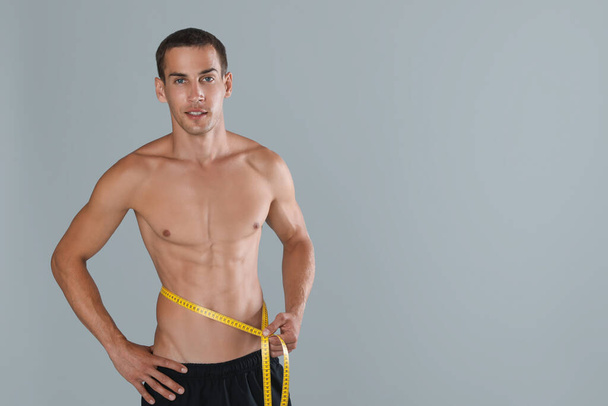 Handsome shirtless man with slim body and measuring tape around his waist on grey background. Space for text - Foto, Imagen