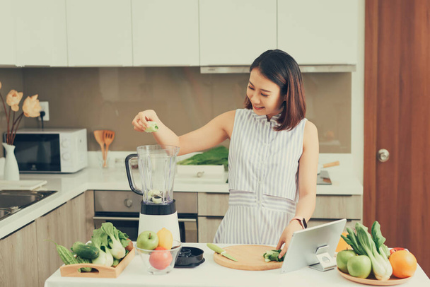 Zdrowa Azjatka cieszyć się co zielone warzywa detox oczyścić i zielony koktajl owocowy z blenderem w kuchni w domu. diety koncept.healthy stylu życia - Zdjęcie, obraz