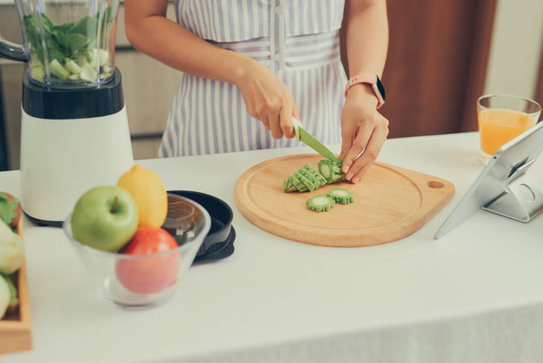 Mujer cortando frutas vs verduras para hacer batidos en la cocina de la receta en la tableta. - Foto, imagen
