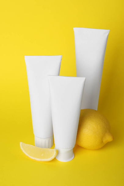 Blank tubes of toothpaste and fresh lemon on yellow background - 写真・画像