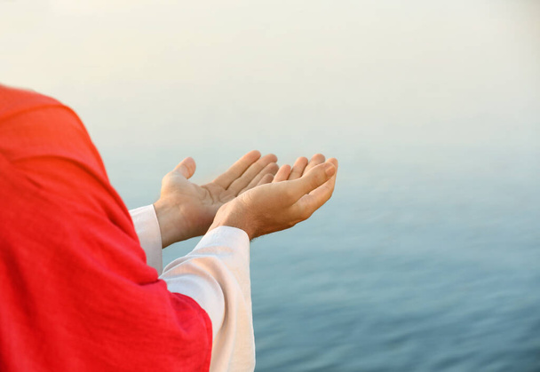 Jesus Christ reaching out his hands near water outdoors, closeup - Zdjęcie, obraz