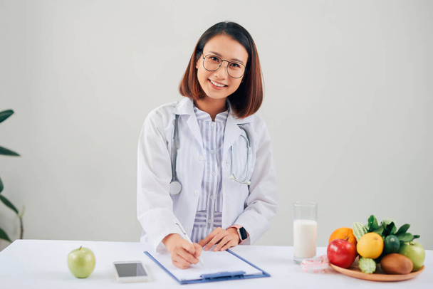 Asian Female nutritionist with fruits working at her desk. Health care and diet concept. - Φωτογραφία, εικόνα
