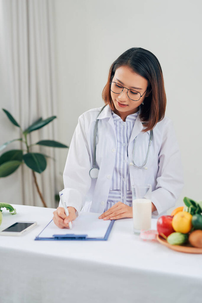 Nutricionista Asiática con frutas trabajando en su escritorio. Concepto de salud y dieta
. - Foto, imagen