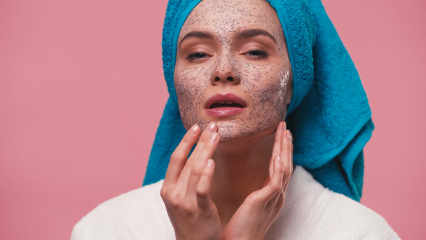 žena s modrým ručníkem na hlavě použití kosmetické drhnutí na tváři izolované na růžové - Fotografie, Obrázek