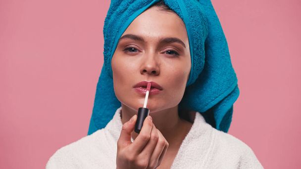 young woman with blue towel on head applying lip gloss isolated on pink - Fotó, kép