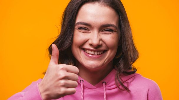 excited woman showing thumb up while looking at camera isolated on yellow - Fotografie, Obrázek