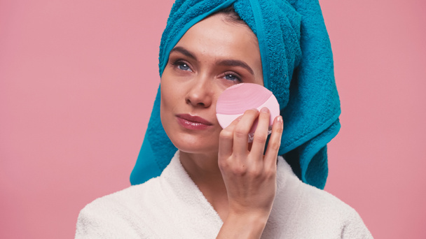 woman with towel on head using silicone cleansing brush on face isolated on pink - Photo, Image