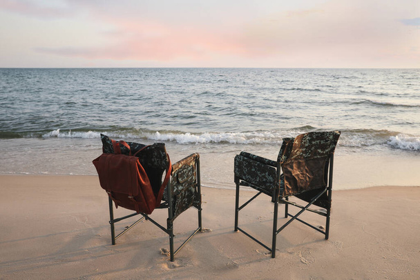 Camping chairs and backpack on sandy beach near sea - Photo, image