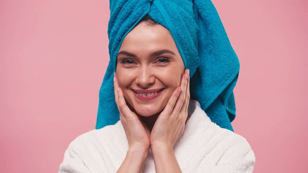 joyful woman with towel on head touching clean face isolated on pink - Photo, image