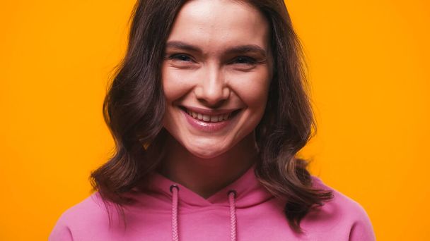 cheerful woman in pink hoodie smiling at camera isolated on yellow - Foto, Imagen