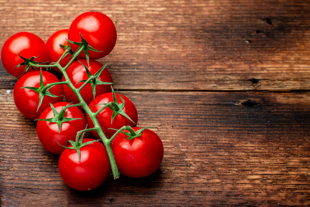 Branch of fresh cherry tomatoes on a brown wooden background. - Fotografie, Obrázek