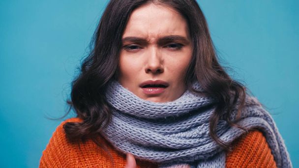 sick woman in warm scarf suffering from pain in sore throat isolated on blue - 写真・画像