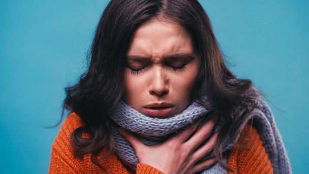 mulher doente em cachecol de malha tosse com olhos fechados isolados em azul - Foto, Imagem