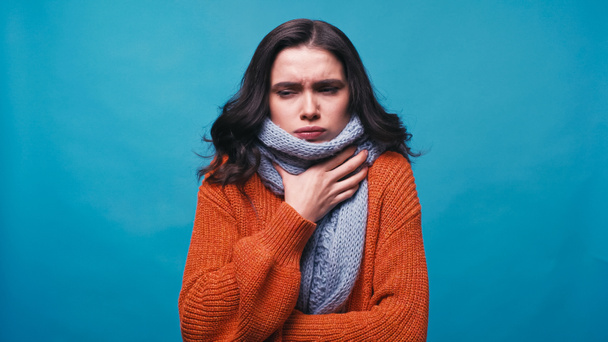 femme malade en écharpe chaude toucher le cou tout en souffrant de douleur dans la gorge isolé sur bleu - Photo, image