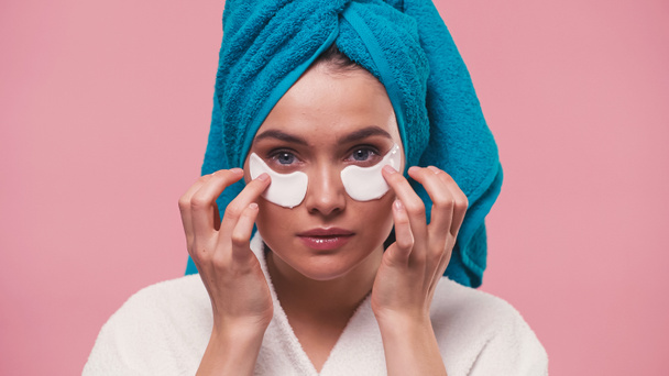 pretty woman with towel on head applying eye patches isolated on pink - Photo, image