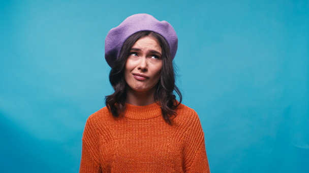 confused woman in lilac beret looking away isolated on blue - Foto, imagen