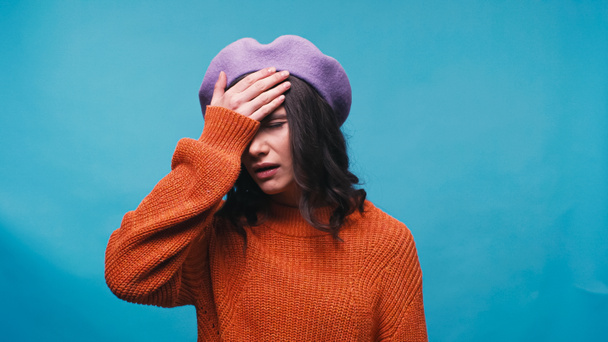 upset woman in beret showing facepalm gesture isolated on blue - Photo, Image