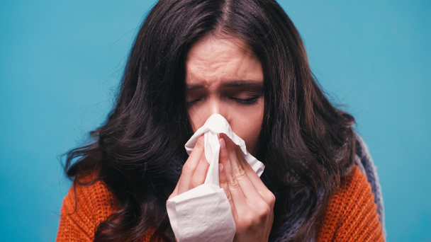 Kranke Frau mit geschlossenen Augen niest in Papierserviette isoliert auf blau - Foto, Bild