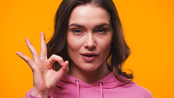 positive woman showing okay gesture while looking at camera isolated on yellow - Foto, Imagem
