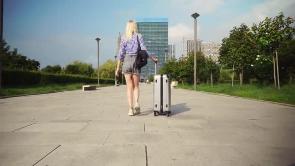 giovane bella donna cammina attraverso la città resort e rotola valigia dietro di lei. - Filmati, video
