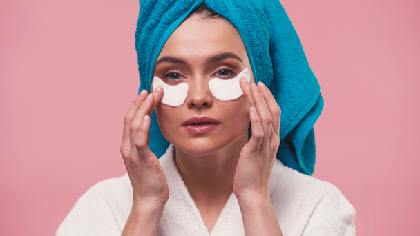 young woman looking at camera while applying eye patches isolated on pink - Foto, imagen