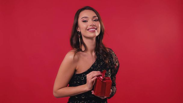 весела і елегантна жінка тримає подарункову коробку ізольовано на червоному
 - Фото, зображення