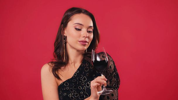 young woman looking at glass of wine isolated on red - Photo, Image