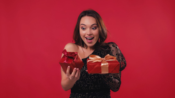 excited young woman holding gift boxes isolated on red - Foto, Imagem
