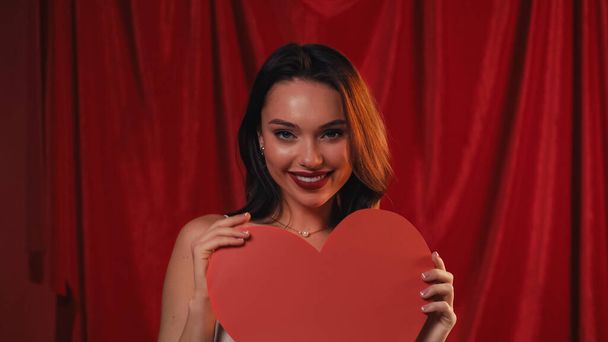 молода і весела жінка тримає паперове серце на червоному
 - Фото, зображення