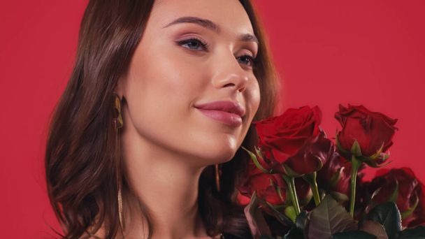 gelukkig jong vrouw ruiken rozen geïsoleerd op rood - Foto, afbeelding
